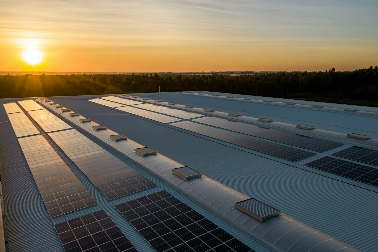 Fotovoltaické panely na střeše průmyslové haly při západu slunce